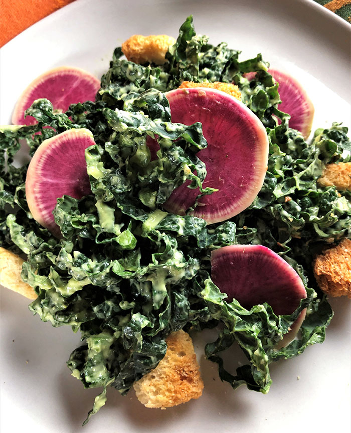 lacinato kale with creamy avocado dressing and watermelon radishes on a white plate