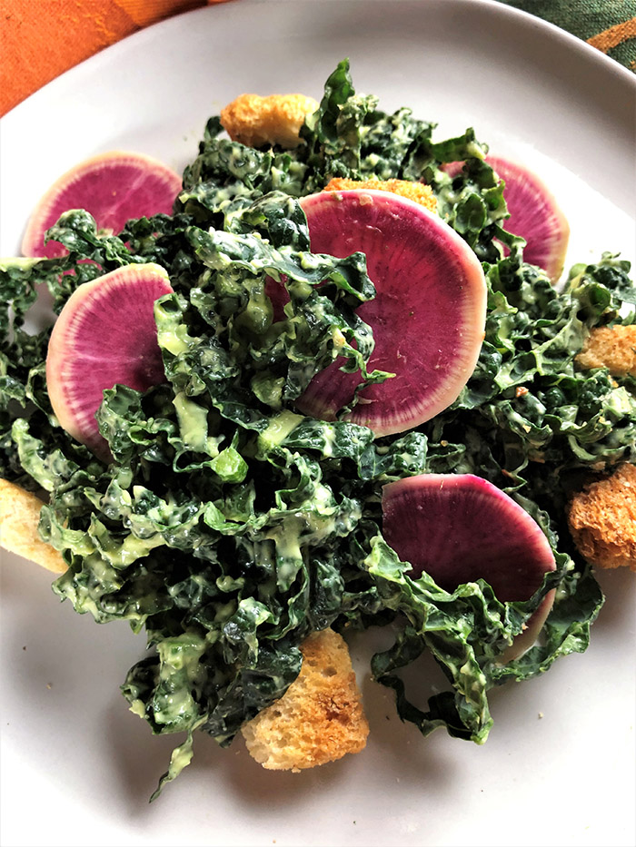 acinato kale with creamy avocado dressing and watermelon radishes on white plate