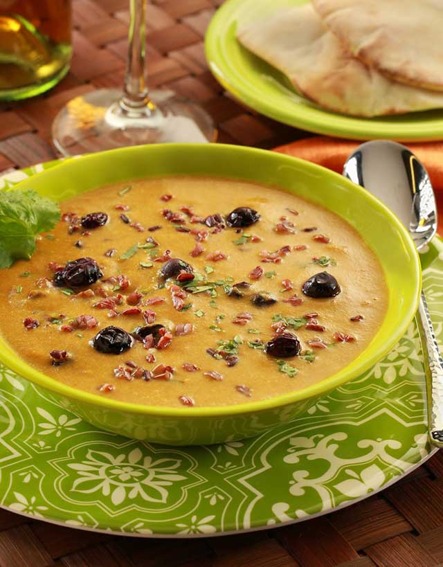 Green bowl with curried mulligatawny soup with roasted blueberies and red rice on a green patterned plate, with spoon and pita bread