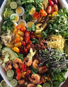 overhead shot of large oval platter with grilled shrimp, avocado, hard boiled eggs, micro greens, tomatoes, corn, bacon. Grilled cobb salad