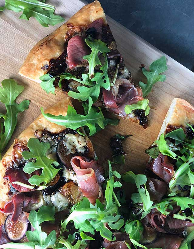 Cutting board with pizza with figs, prosciutto, arugula and gorgonzola