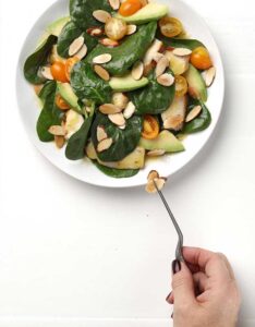 Hand with tweezers adding almonds to a spinach, almond, orange salad