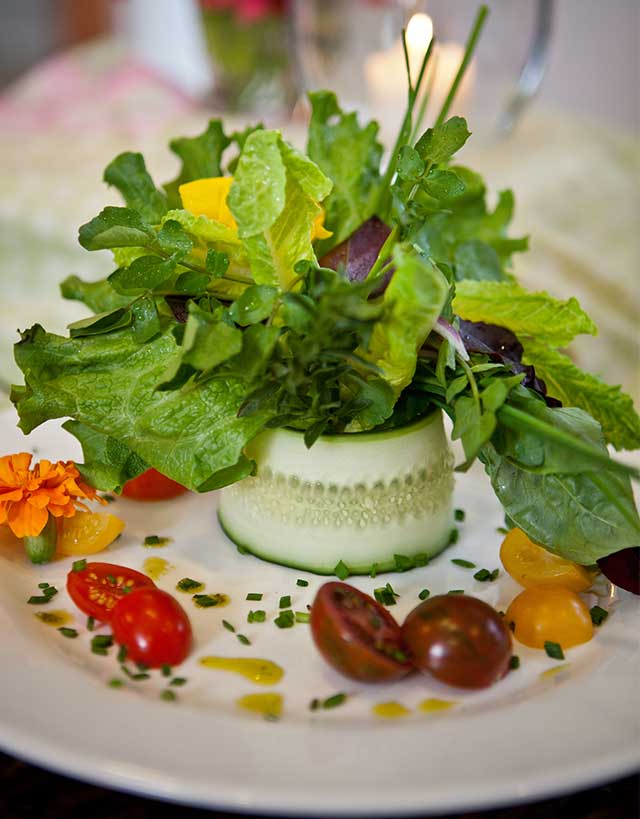 Composed salad banded with a cucumber slice, on a white plate with cherry tomatoes