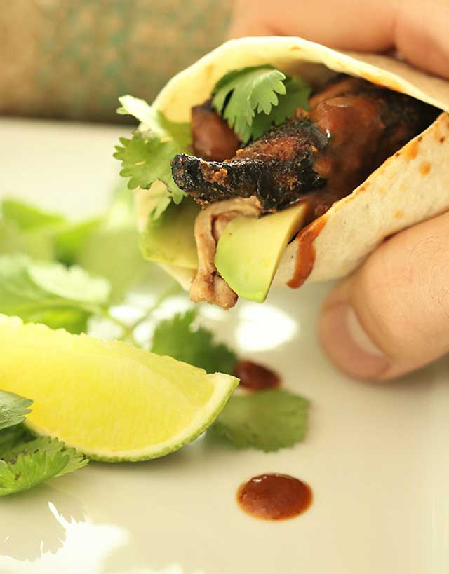 Hand holding a tortilla filled with fig glazed chicken thighs, with cilantro and lime wedge